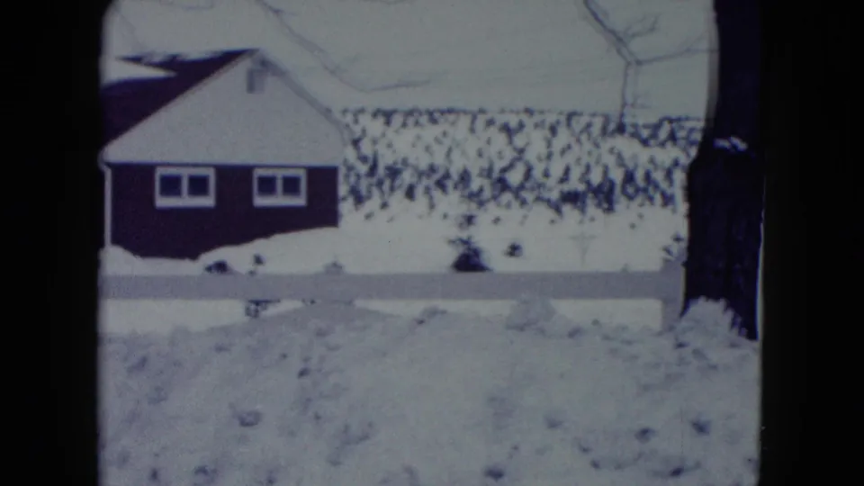 1960 Madison, Wisconsin frame with a dark suburban house beyond a snow-filled yard, low white fence, and bare branches.