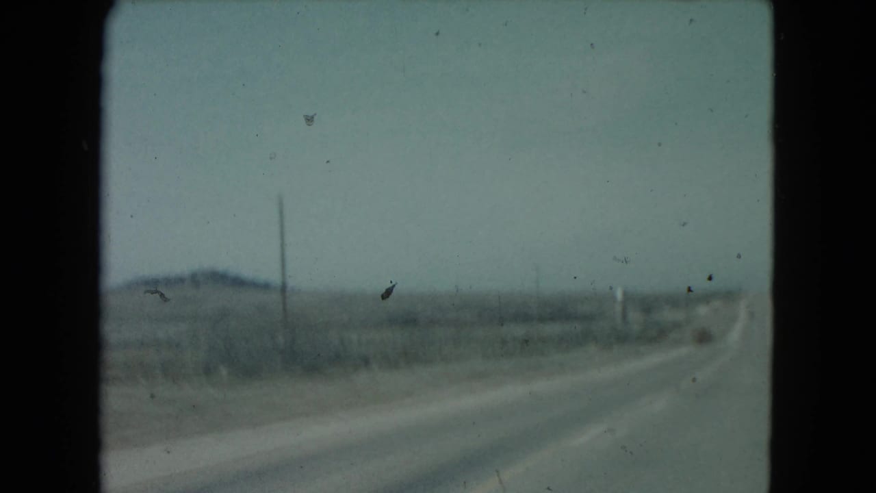 1960 Nevada road view with a long highway receding through arid plains, sparse poles, and distant hills.