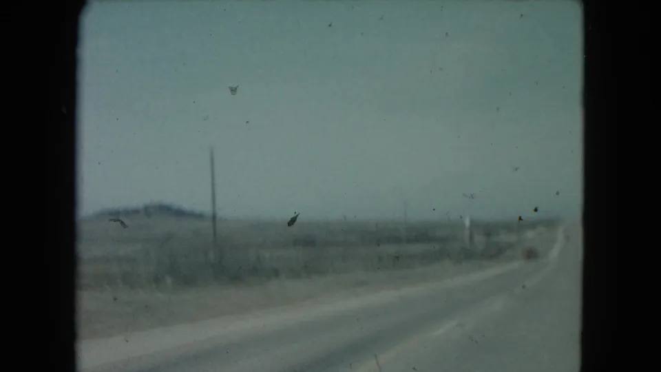 1960 Nevada road view with a long highway receding through arid plains, sparse poles, and distant hills.