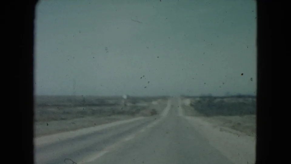 1960 Nevada vehicle-view frame showing a paved highway running toward the horizon through flat desert with low vegetation.