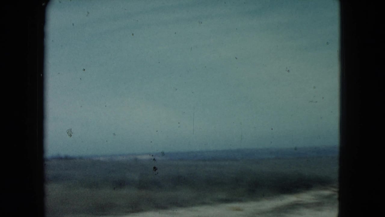 Soft view across open countryside from a moving vehicle, with sky, low horizon, and film gate edges.