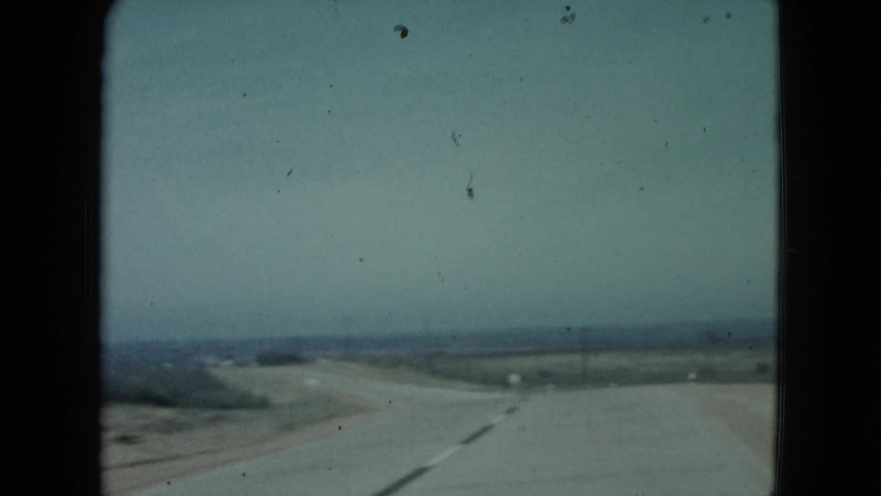 Paved rural road curving through open desert beneath a hazy sky.