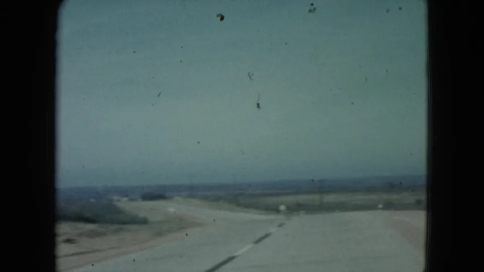 1960 Nevada 8mm frame showing a paved road bending across flat desert terrain under a pale, hazy sky.