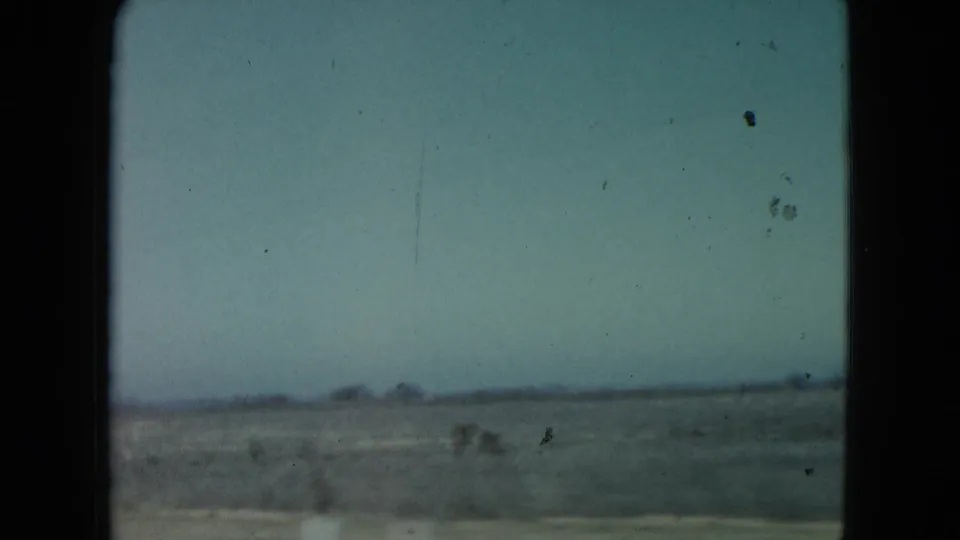 End frame of the 1960 Nevada home movie drive, showing sparse desert scrub and distant low landforms under a hazy sky.