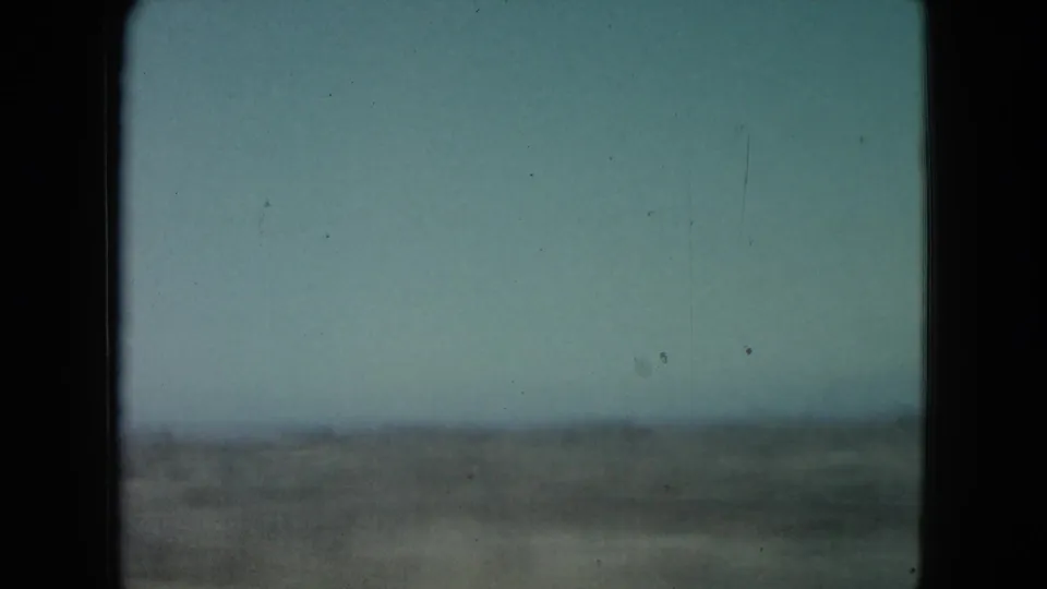 Muted 1960 Nevada landscape frame showing a blurred brown field and low horizon from a moving vehicle.