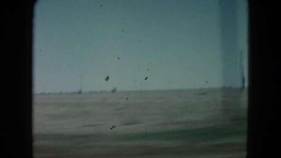 Passing 8mm road view in Nevada with distant utility poles, scrubby brush, and a flat rural horizon.
