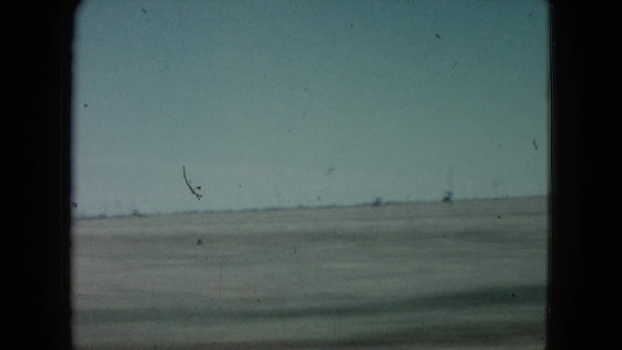 Flat desert horizon under a pale sky with distant structures barely visible.