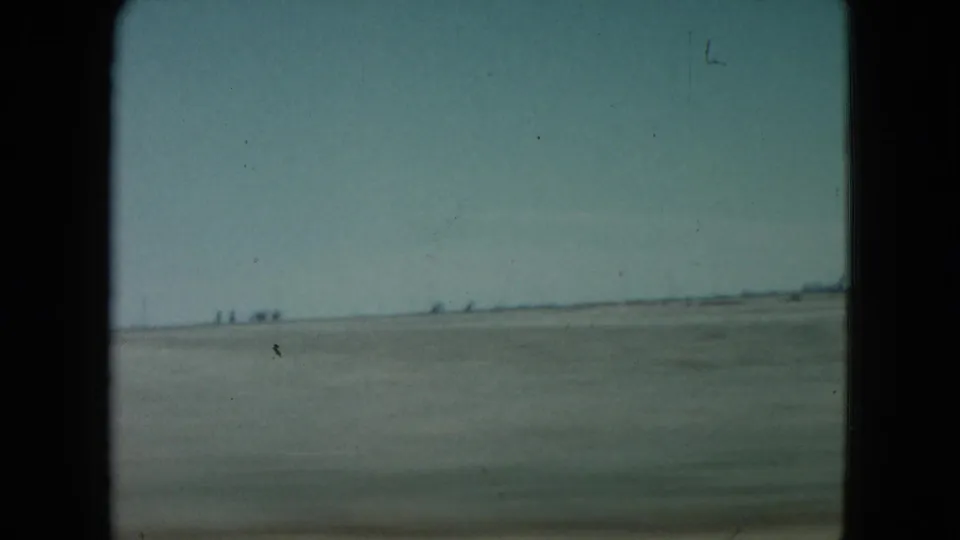 1960 Nevada 8mm frame showing a sparse desert plain, low horizon, small distant shapes, and visible film grain.