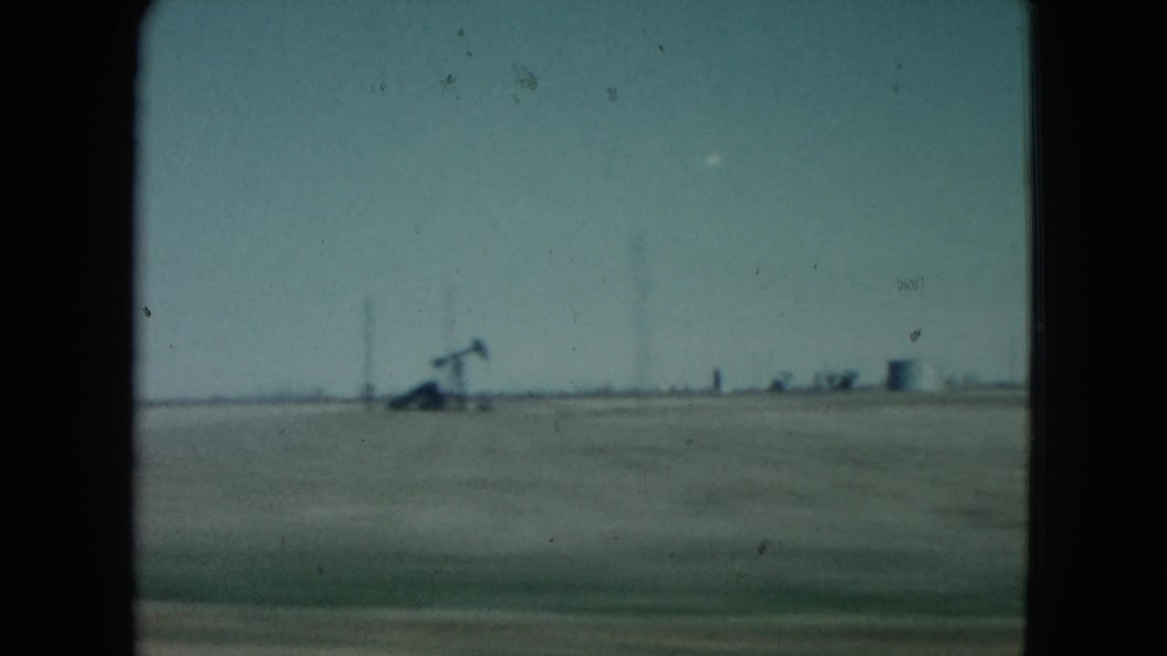 1960 Nevada 8mm frame showing flat open plains with distant oil pumpjacks beyond a dark car-window border.