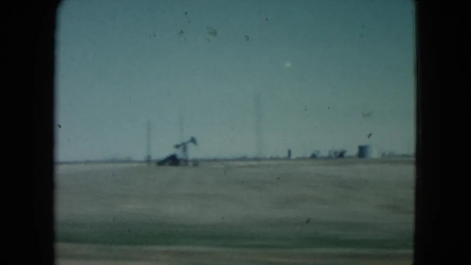 1960 Nevada 8mm frame showing flat open plains with distant oil pumpjacks beyond a dark car-window border.