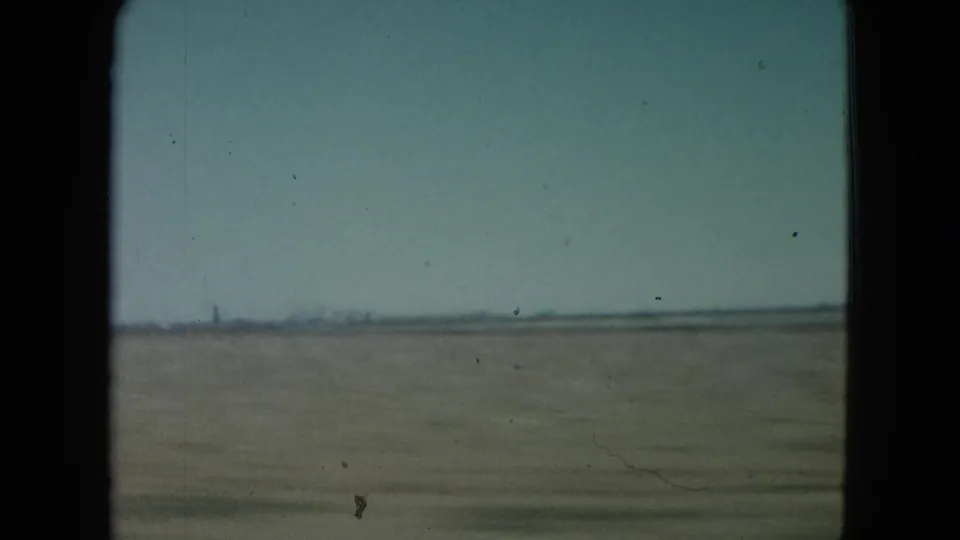 1960 Nevada 8mm frame showing open plains from a moving vehicle, with a faint horizon and dark window border.