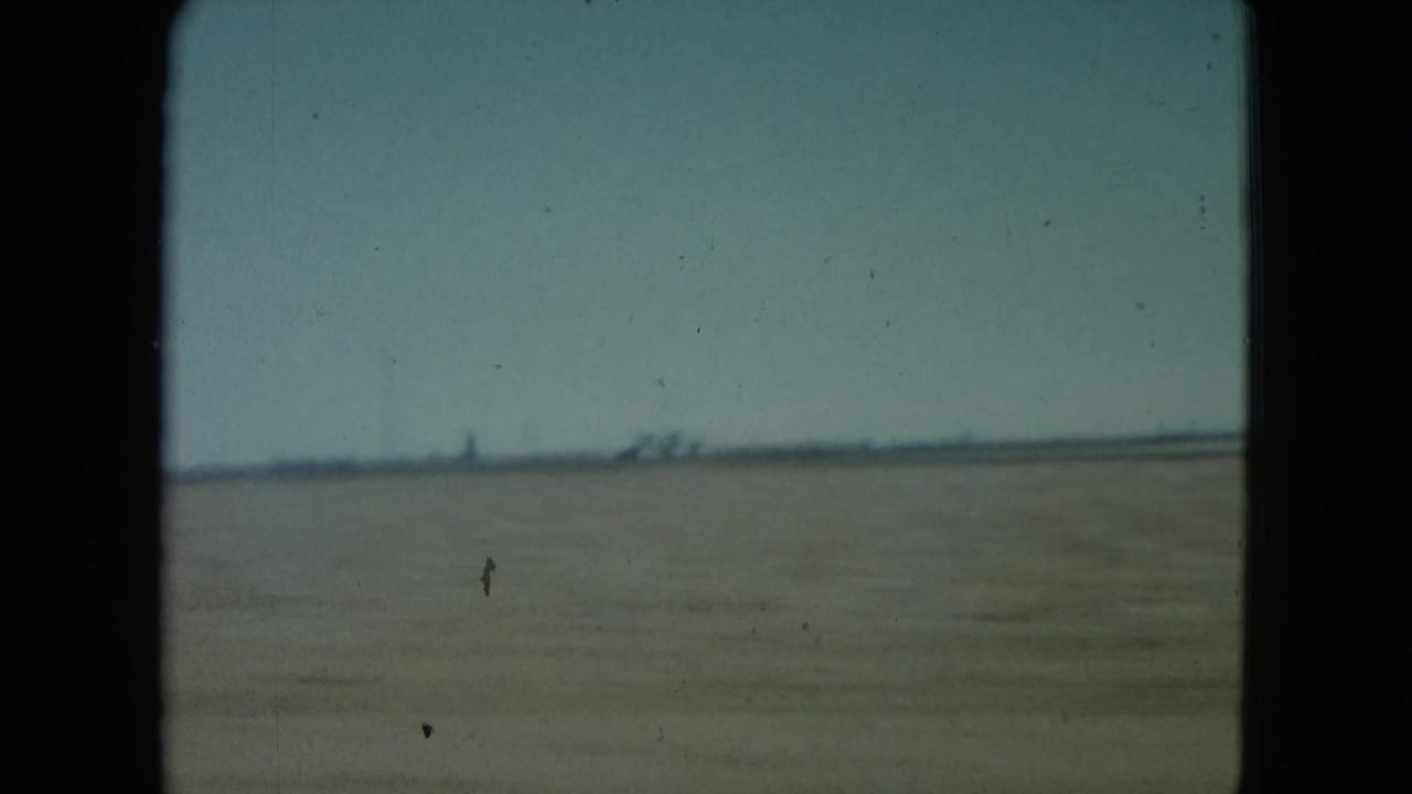 Flat desert landscape seen through a vehicle window with a distant horizon under pale sky.