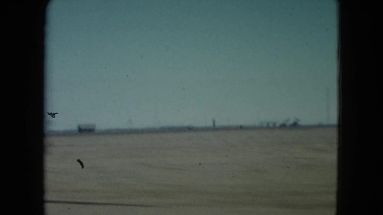 Open desert horizon with distant structures framed by dark film borders.