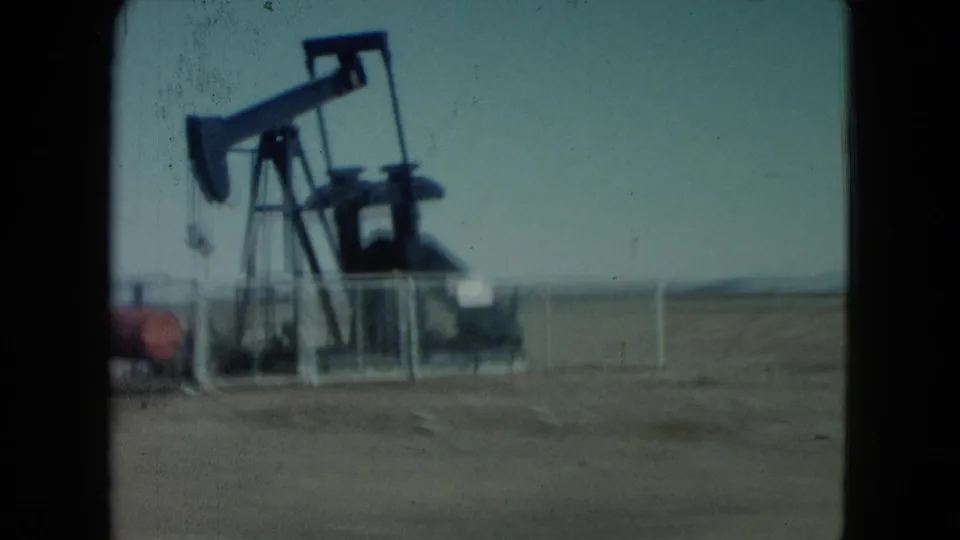 A roadside oil pump jack appears in the Nevada desert, filmed from a moving vehicle on 8mm home-movie stock in 1960.