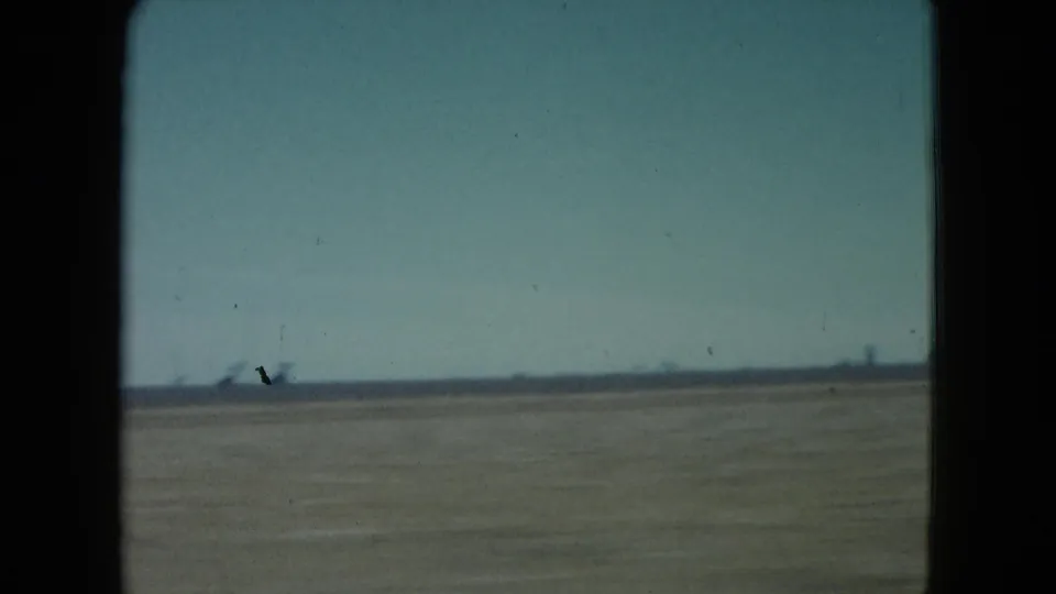 1960 Nevada home-movie view of a flat open field from inside a moving vehicle, with dark window edges and distant horizon detail.