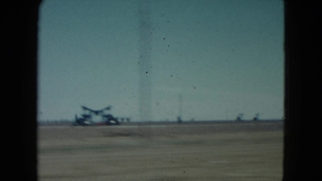 1960 Nevada roadside view with a blurred aircraft-like silhouette and small distant forms across a flat open field.