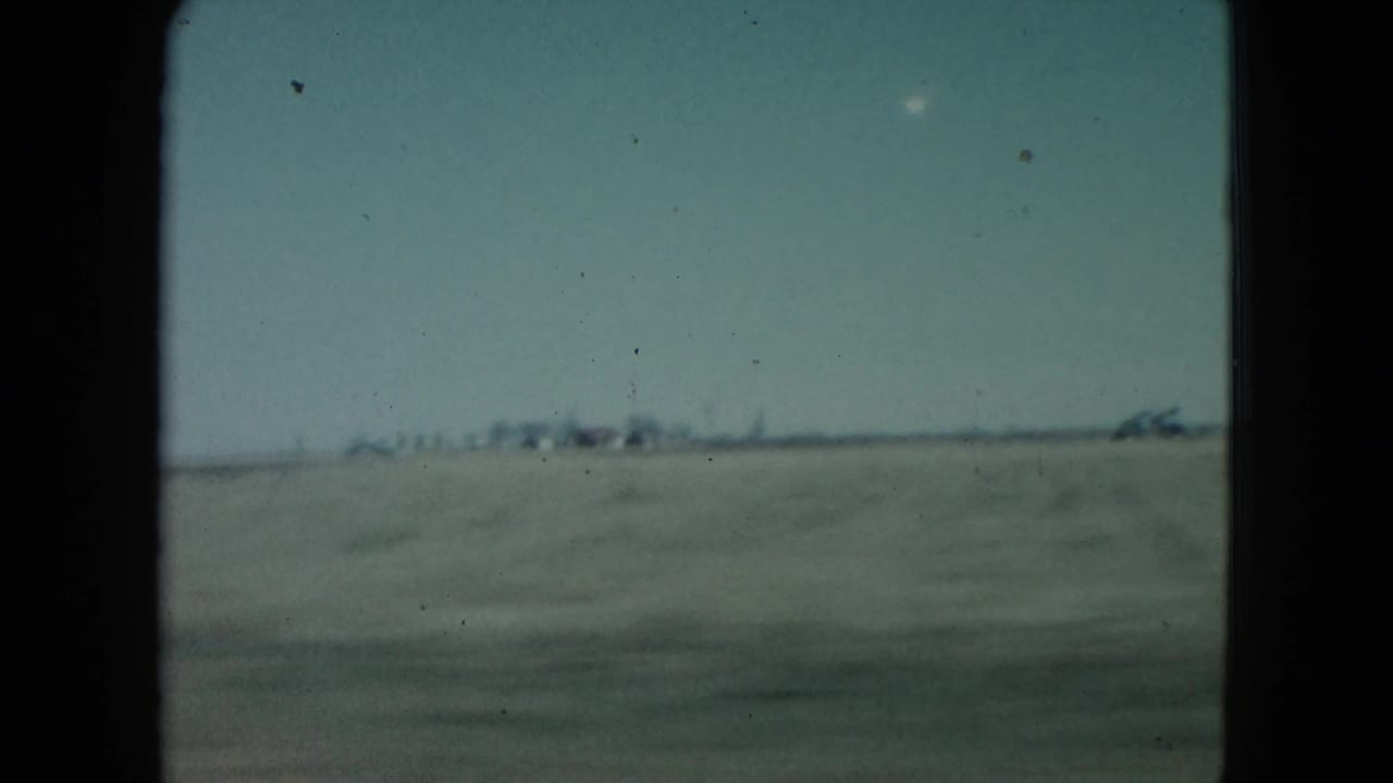 Open field and sky with small distant buildings or poles along the horizon.