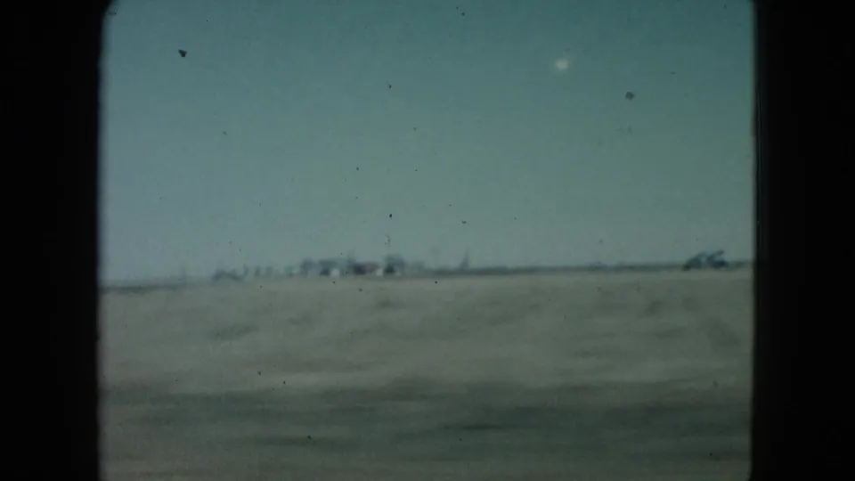 1960 Nevada roadside view with a broad field, pale sky, and small distant structures along the horizon.
