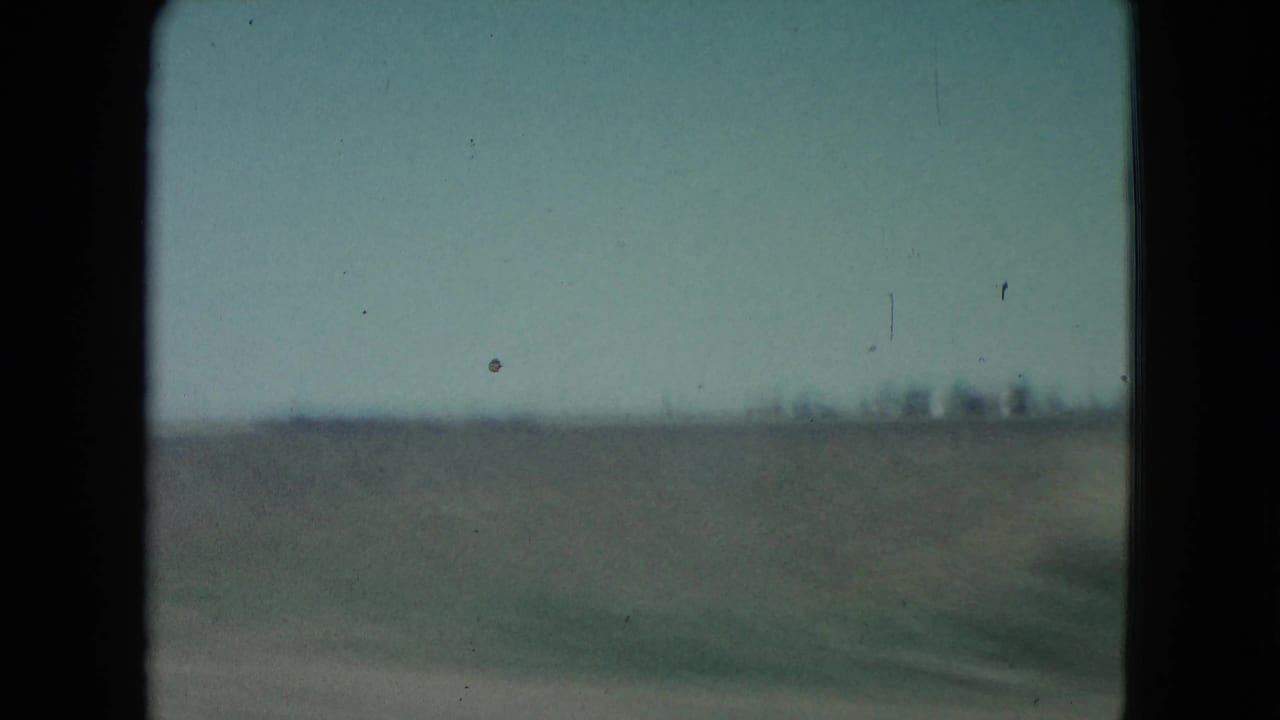 1960 Nevada 8mm frame with motion-blurred field, low horizon, and faint distant structures.