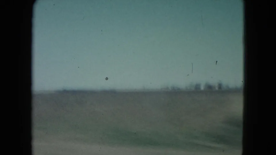 1960 Nevada 8mm frame with motion-blurred field, low horizon, and faint distant structures.
