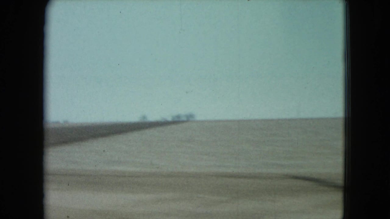 A blurred roadside strip and wide, flat farmland pass the camera, reinforcing the moving passenger perspective in rural Nevada.