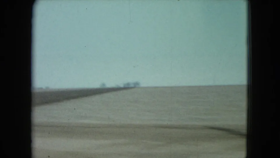A blurred roadside strip and wide, flat farmland pass the camera, reinforcing the moving passenger perspective in rural Nevada.