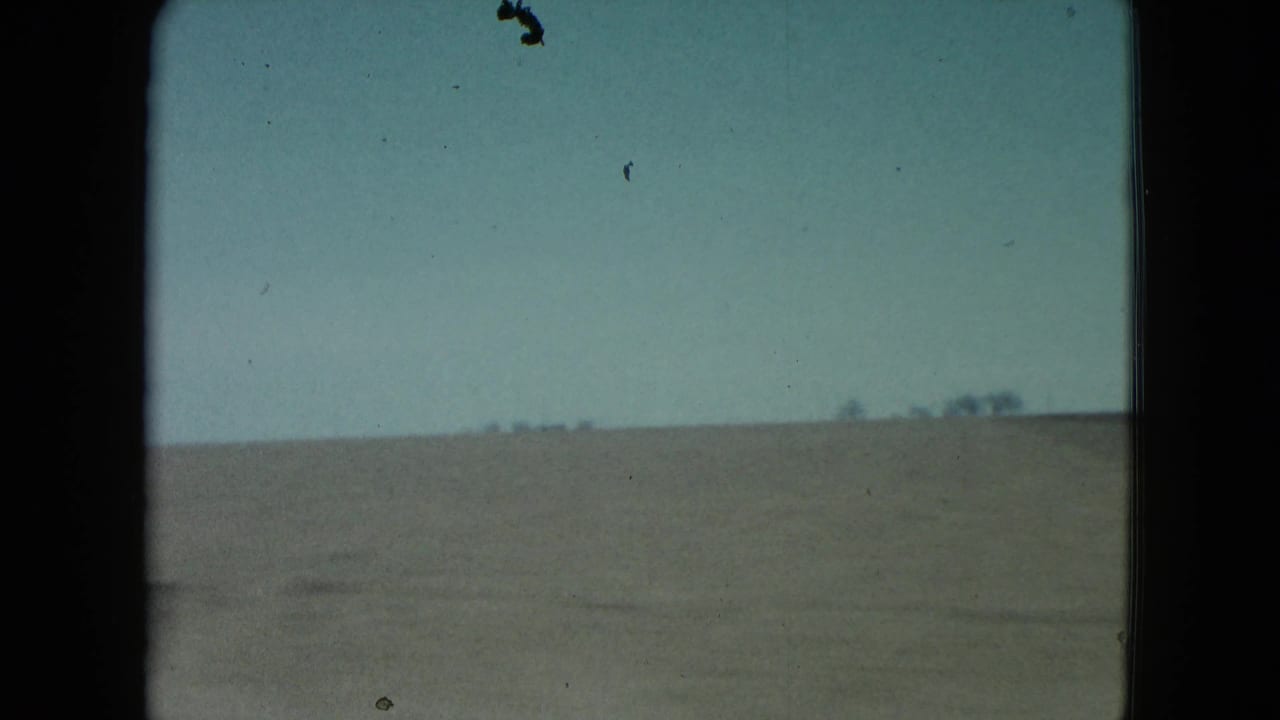Open rural Nevada field stretches to a low horizon with small distant trees, seen through faded 8mm color and dark film-frame borders.