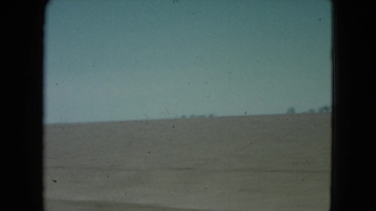 1960 Nevada 8mm frame showing a flat barren desert horizon beneath a pale blue sky, bordered by dark film gate edges.