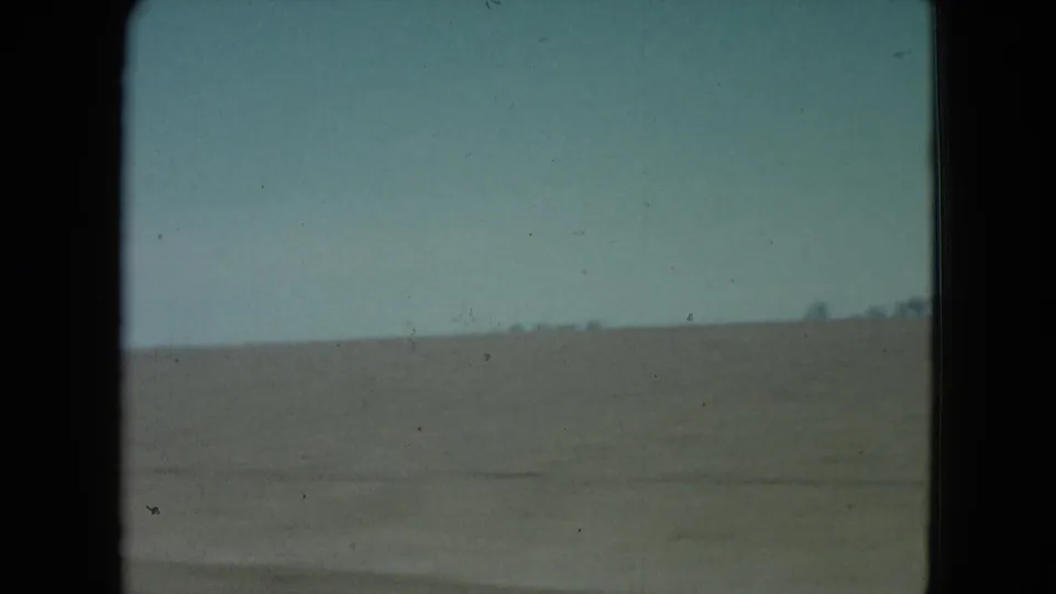 1960 Nevada 8mm frame showing a flat barren desert horizon beneath a pale blue sky, bordered by dark film gate edges.