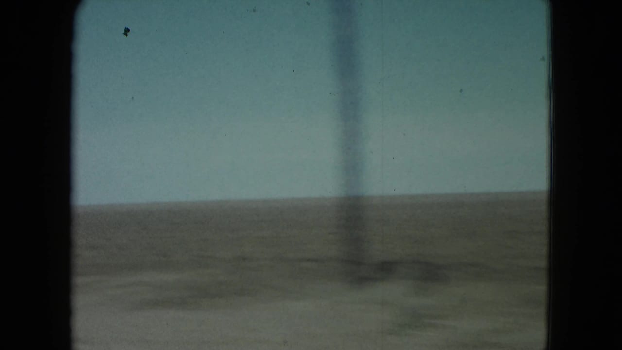 1960 Nevada 8mm frame with a blurred roadside utility pole passing in front of a flat desert plain and blue sky.