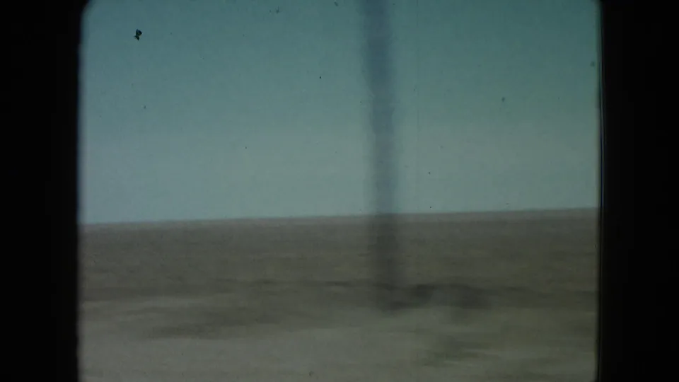 1960 Nevada 8mm frame with a blurred roadside utility pole passing in front of a flat desert plain and blue sky.
