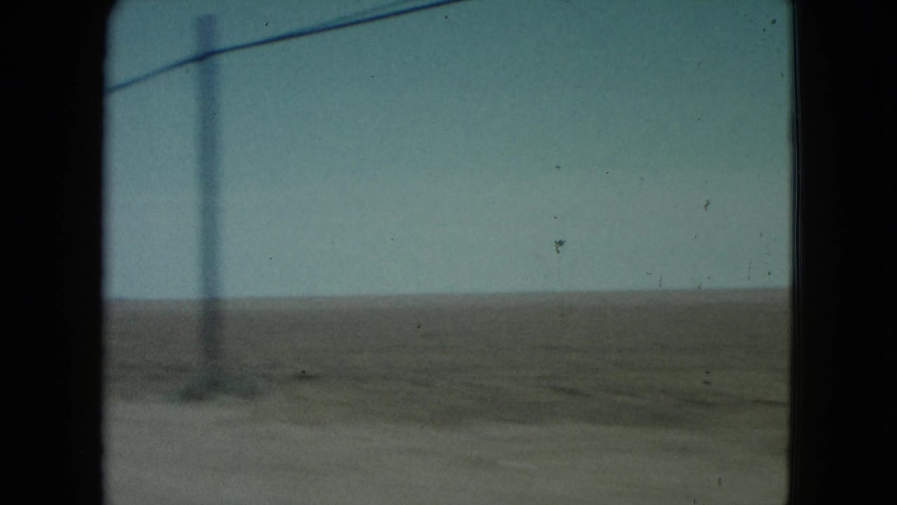 1960 Nevada 8mm frame showing a utility pole and overhead line against a pale sky above barren desert terrain.