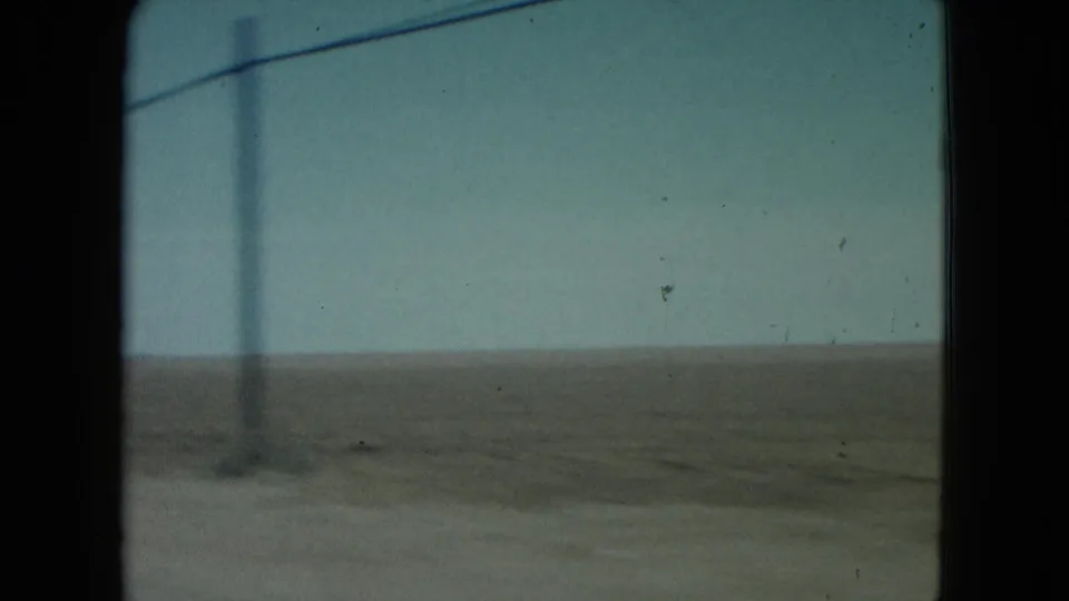 1960 Nevada 8mm frame showing a utility pole and overhead line against a pale sky above barren desert terrain.