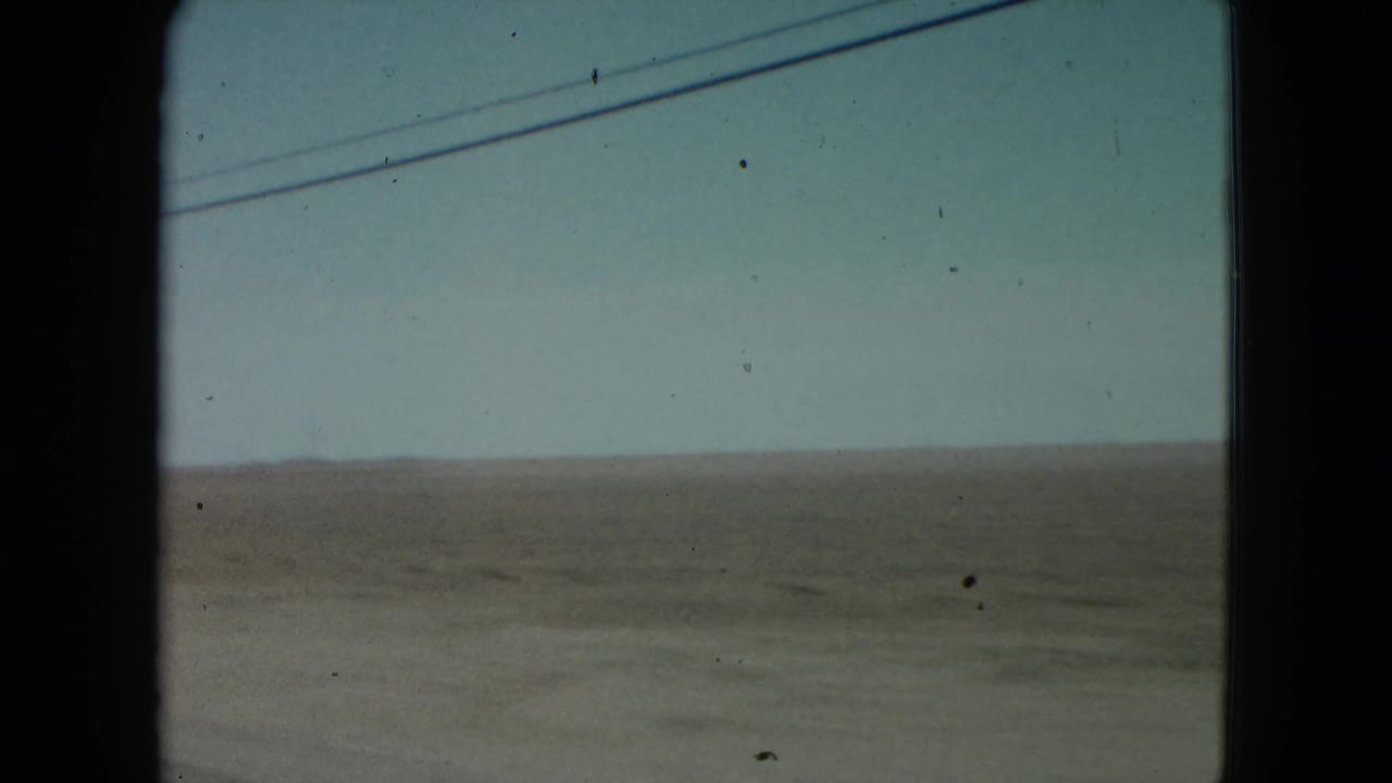 1960 Nevada 8mm home-movie frame looking through a car window toward flat countryside and overhead wires.