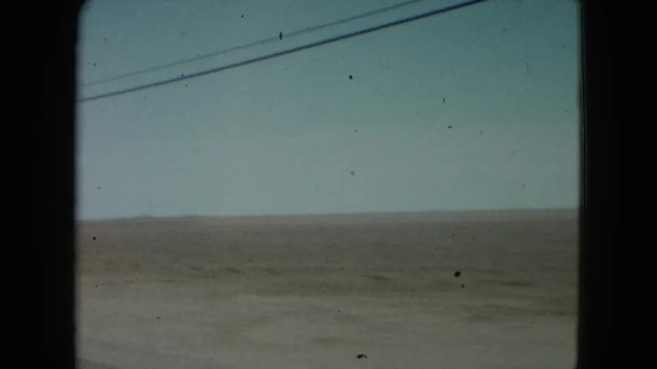 1960 Nevada 8mm home-movie frame looking through a car window toward flat countryside and overhead wires.
