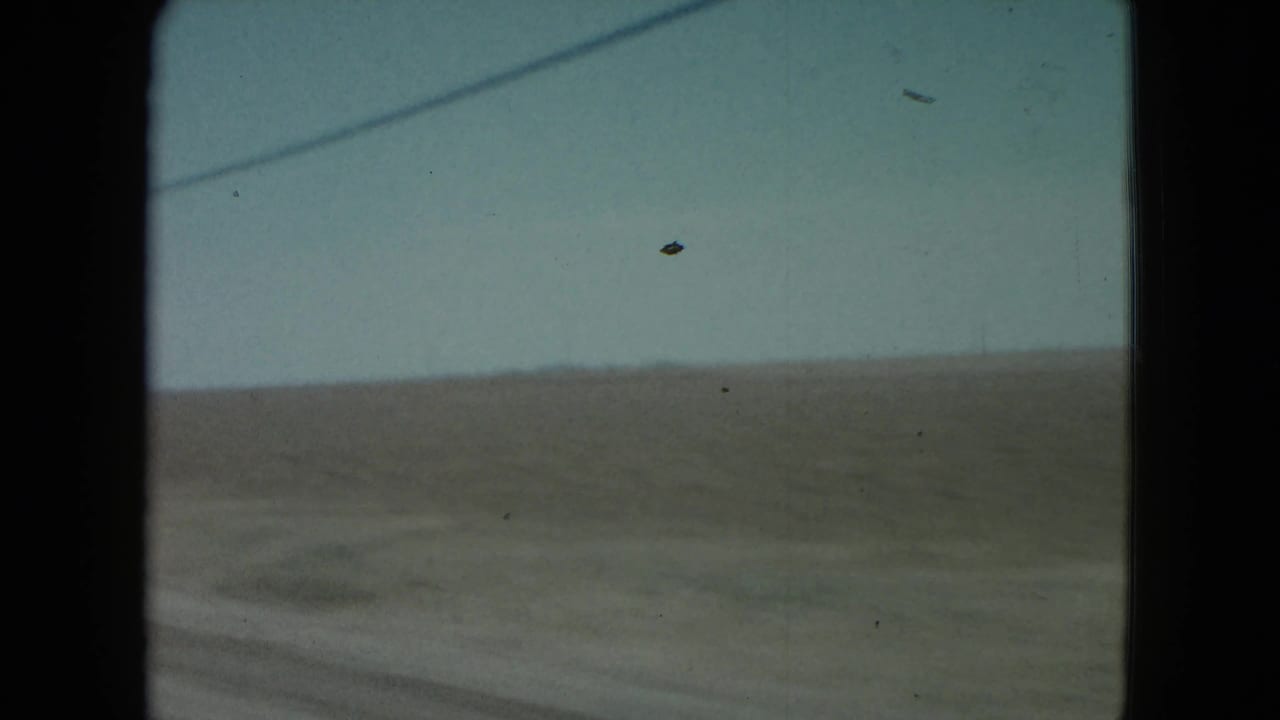 Open rural landscape seen through a vehicle window with a faint road or track below.