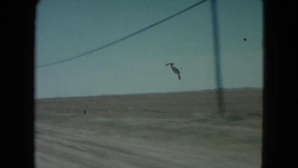 1960 Nevada 8mm frame from a moving car showing a utility pole, wires, and open rural terrain.