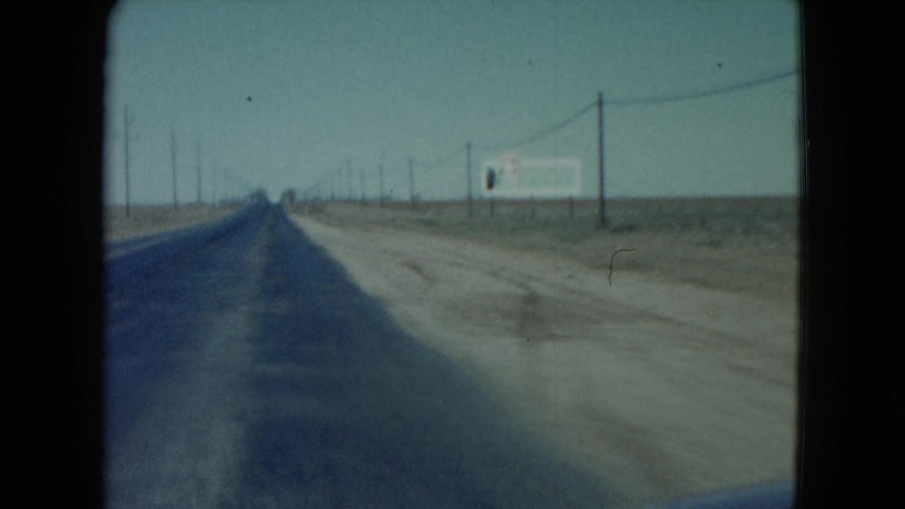 Straight paved highway receding into flat desert with utility poles and a roadside sign at right.