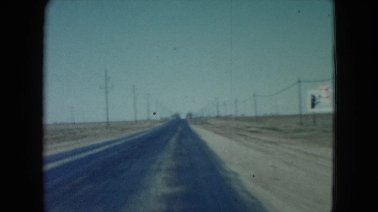 1960 Nevada 8mm frame from a moving car shows a paved highway, dirt roadside, utility poles, overhead wires, and a partially visible sign.