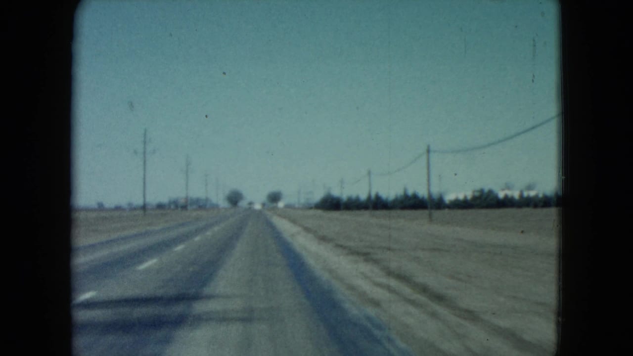 Empty straight highway with utility poles and wires running along flat land.