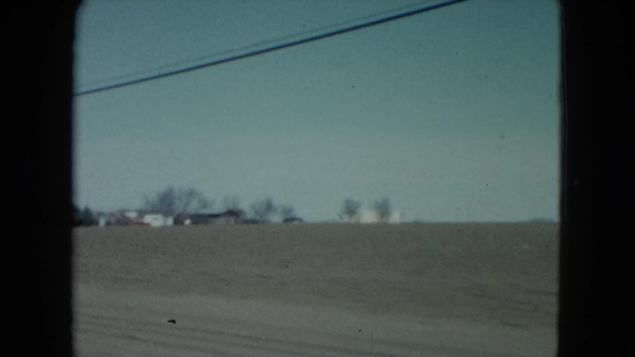 Flat farmland with distant houses and a power line crossing the upper frame.