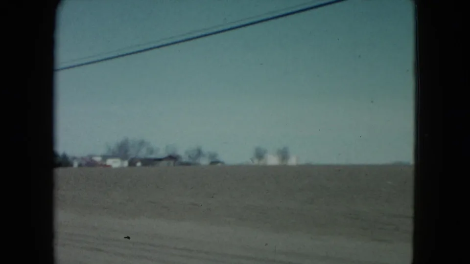 1960 Nevada countryside passing view with open fields, low houses near the horizon, and an overhead power line.