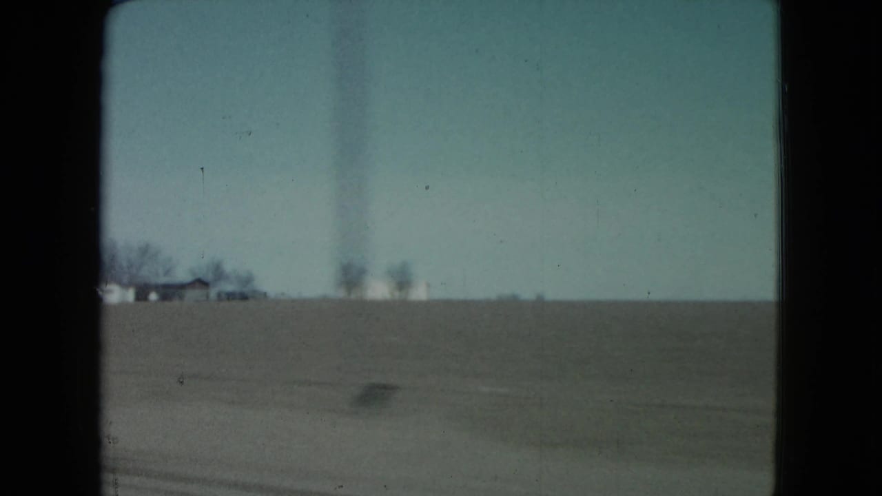 1960 Nevada farmland view from a moving vehicle, with distant houses, bare trees, and motion blur near the roadside.