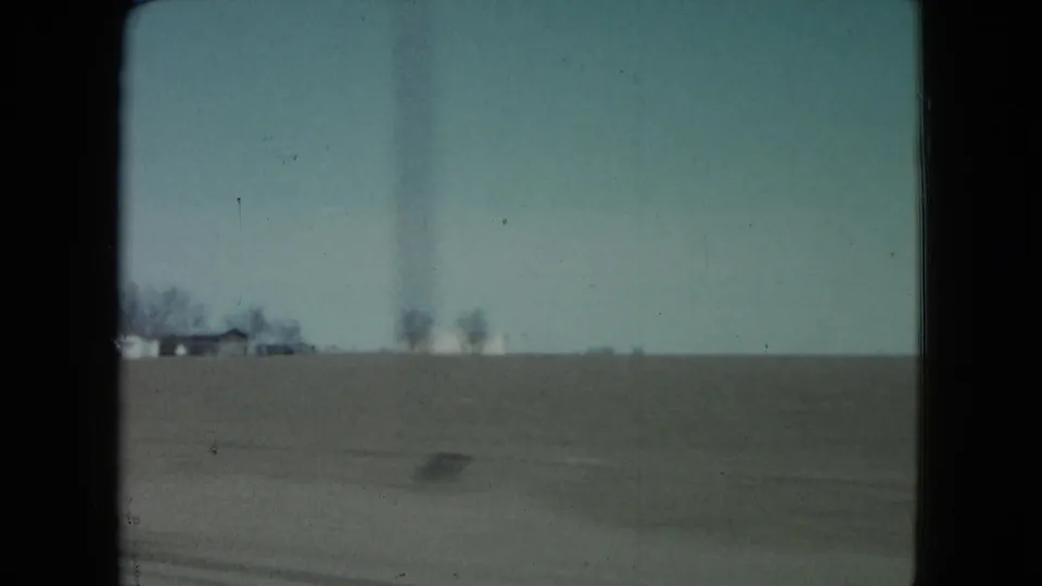 1960 Nevada farmland view from a moving vehicle, with distant houses, bare trees, and motion blur near the roadside.