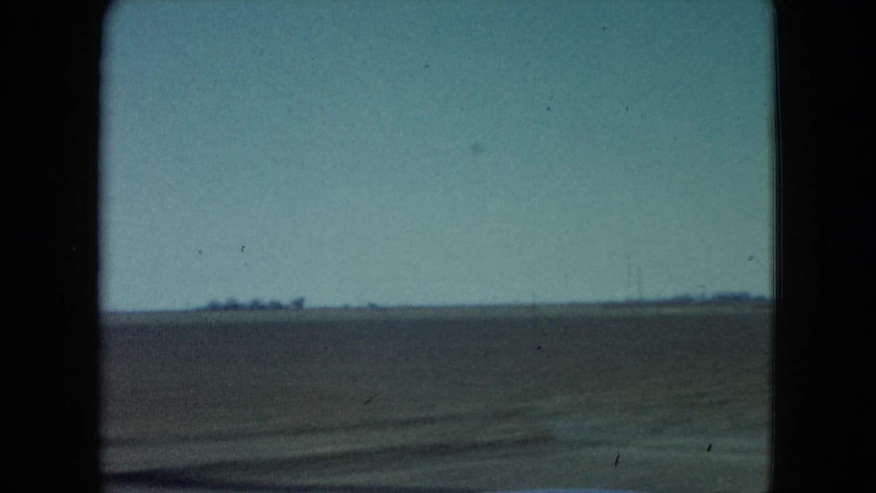 1960 Nevada rural landscape with a broad field, distant utility poles, low horizon, and vehicle-motion blur in the foreground.