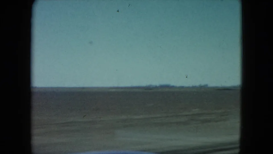 1960 Nevada home-movie frame showing arid open land through a moving car window, with a low horizon and pale blue sky.