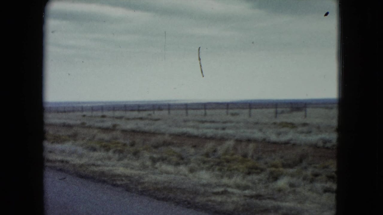 1960 Nevada home-movie view of a flat roadside plain, fence line, and cloudy sky from a moving vehicle.