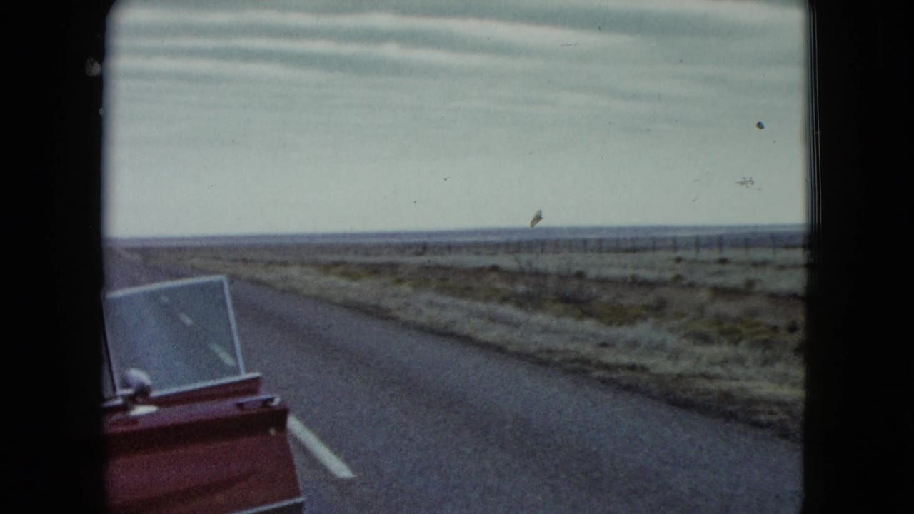 The red car door and open window enter the frame beside a quiet Nevada road and open plain.
