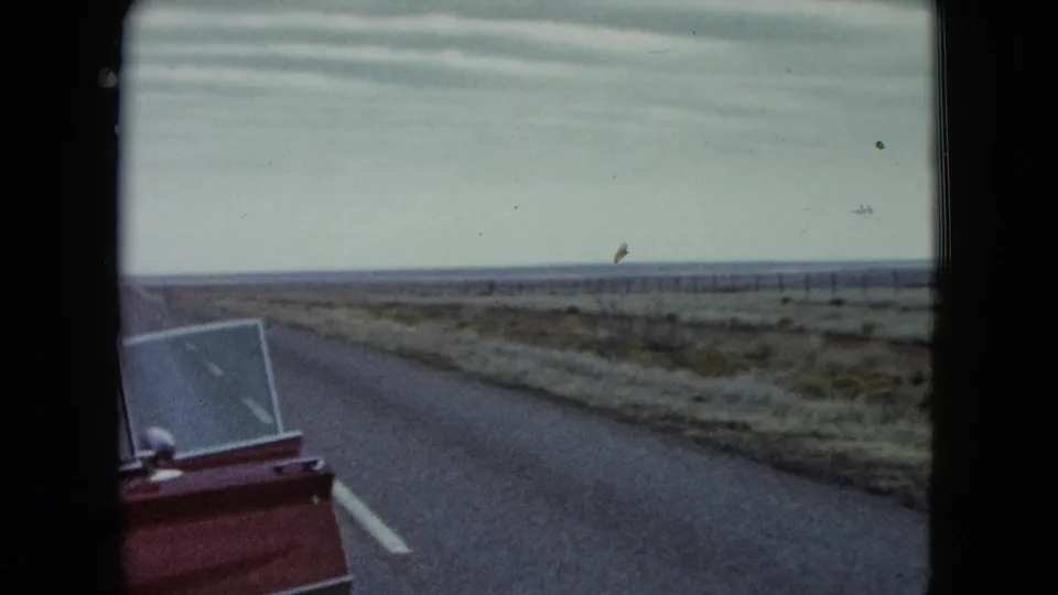 The red car door and open window enter the frame beside a quiet Nevada road and open plain.