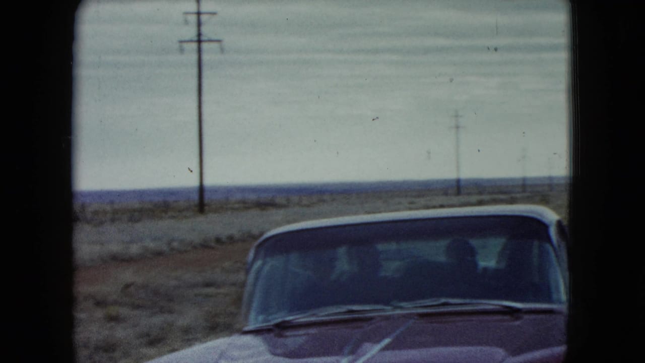 1960 Nevada roadside frame with the front of a red car at the edge of a sparse highway landscape.